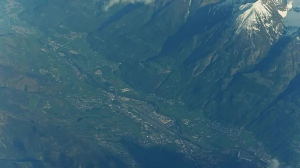 Picos de montaña, aeropuerto distante y pueblos alpinos en un valle — Foto de Stock