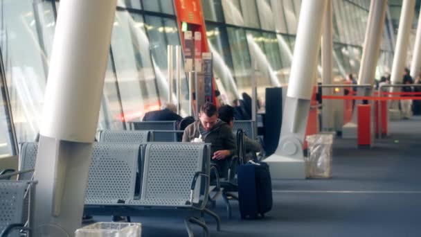 WARSAW, POLAND - APRIL, 14, 2017. Steadicam shot of young man using his smartphone and eating ice cream at airport terminal. 4K clip — Stock Video
