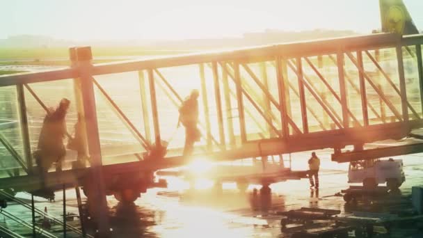 WARSAW, POLONIA - 14 DE ABRIL DE 2017. Siluetas de pasajeros con maletas caminando en un puente elevado de cristal. Dejando un avión en el aeropuerto contra el atardecer. Disparo 4K — Vídeos de Stock