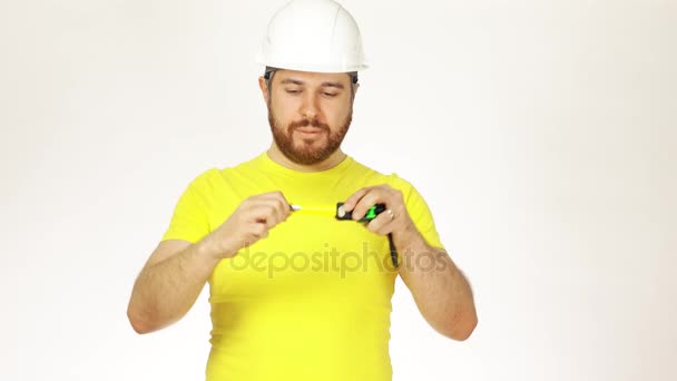 Ingeniero de construcción alegre o arquitecto en camiseta amarilla y sombrero duro usando cinta métrica sobre fondo blanco. Vídeo 4K — Vídeos de Stock