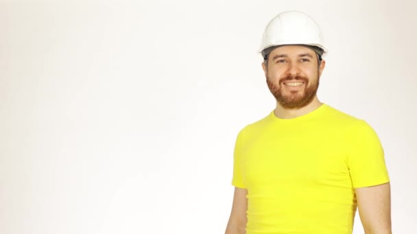 Portrait d'un bel ingénieur de construction souriant ou d'un architecte en tshirt jaune et casque sur fond blanc. Coup 4K — Video