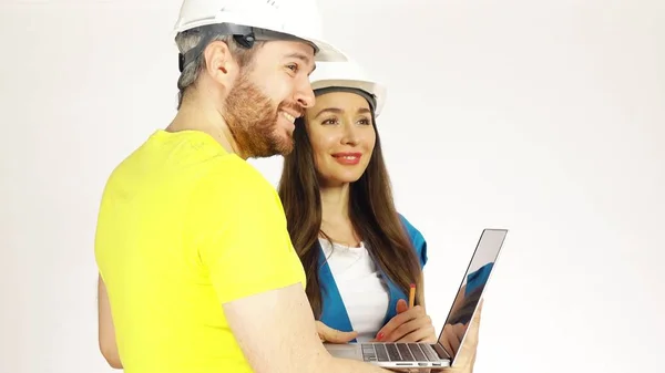 Два инженера или архитектора в шляпах обсуждают проект и используют ноутбук на светлом фоне — стоковое фото