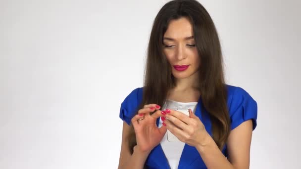Schöne junge brünette Frau, die SMS auf ihrem Handy vor weißem Hintergrund tippt. 4k-Video — Stockvideo