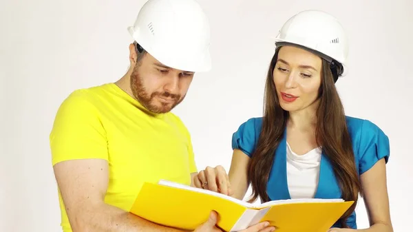Два инженера или архитектора в шляпах обсуждают проект и просматривают документы в желтой папке — стоковое фото