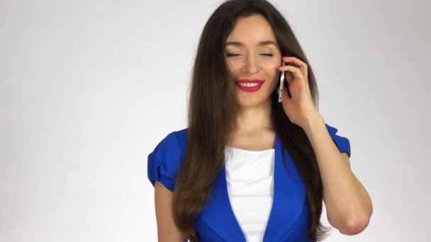 Schöne junge brünette Frau, die auf ihrem Handy vor weißem Hintergrund spricht. 4k-Clip — Stockvideo