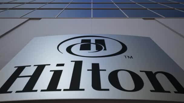 Tablero de señalización exterior con el logotipo de Hilton Hotels Resorts. Moderno edificio de oficinas. Representación Editorial 3D — Vídeo de stock
