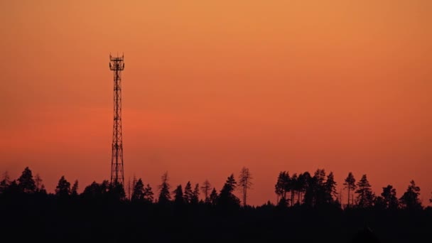 Silueta de una torre celular contra el cielo anaranjado al atardecer. Vídeo 4K — Vídeo de stock