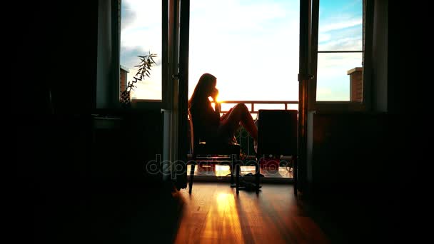 Silhouet van een mooi meisje praten op haar mobiel thuis. 4k video — Stockvideo