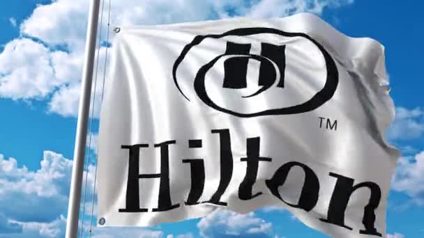 Mengayunkan bendera dengan logo Hilton melawan awan bergerak. Animasi editorial 4K — Stok Video