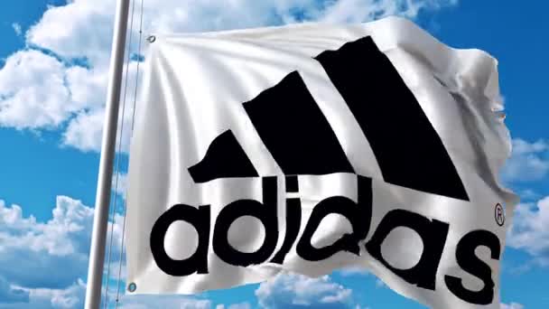 Bandiera sventolante con logo Adidas contro nuvole in movimento. Animazione editoriale 4K — Video Stock