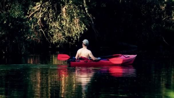 Homem desconhecido em caiaque vermelho flutuando pelo rio e observando as margens dos rios da floresta. Tiro em câmara lenta — Vídeo de Stock