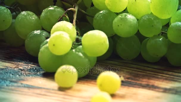 Spraying water over ripe fresh green grapes on a wooden table. Close-up slow motion shot — Stock Video