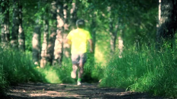 Filmagem em câmera lenta de um atleta desfocado correndo na floresta, visão traseira — Vídeo de Stock