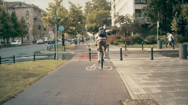 Молодой человек с рюкзаком едет на велосипеде по городской велосипедной дорожке — стоковое фото
