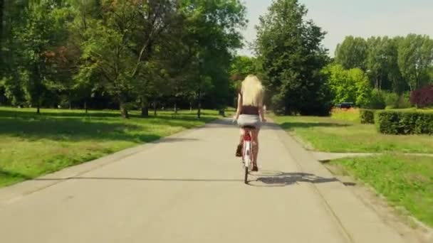 Mujer rubia desconocida en bicicleta a lo largo del camino del parque — Vídeos de Stock