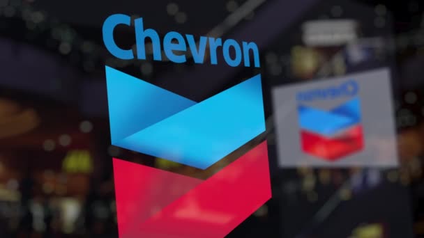 Логотип Chevron Corporation на стекле против размытого бизнес-центра. Редакционная 3D рендеринг — стоковое видео