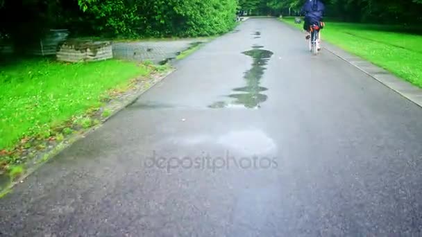 Mujer desconocida en bicicleta a lo largo del camino del parque después de la lluvia de verano — Vídeos de Stock