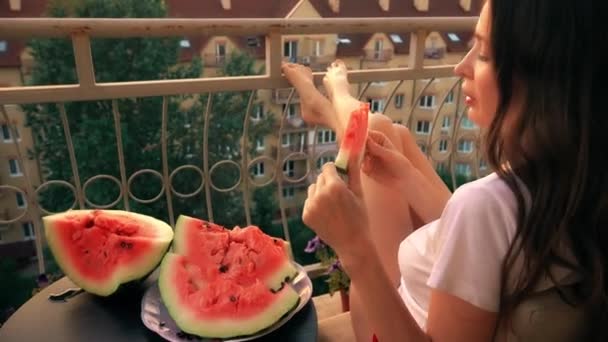 Hermosa mujer morena alegre comiendo sandía en una terraza en casa. Noche de verano tiempo de placer — Vídeo de stock