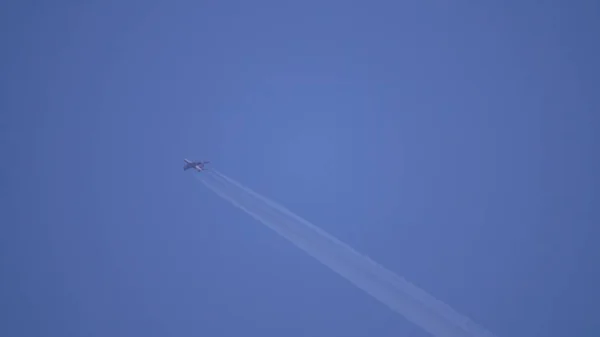 Gran avión comercial de cuatro motores que sale de contrail alto en el cielo azul. Lente de teleobjetivo disparada —  Fotos de Stock