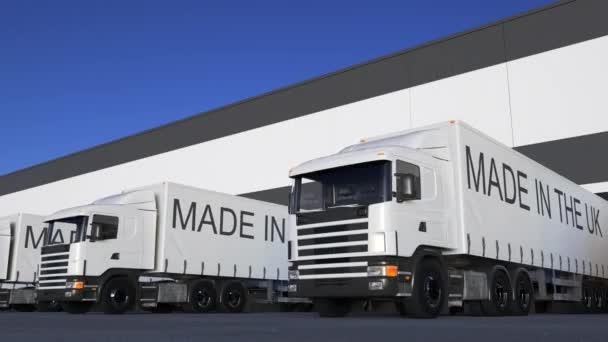 Freight semi trucks with MADE IN THE UK caption on the trailer loading or unloading. Road cargo transportation. Seamless loop 4K clip — Stock Video