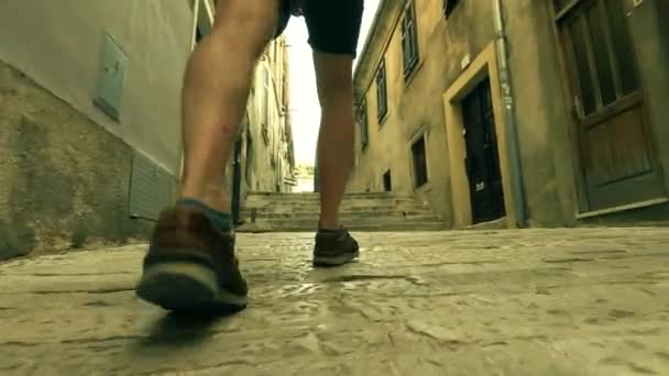 男性旅行者の足、背面図。古代の地中海都市通りに沿って歩く — ストック動画