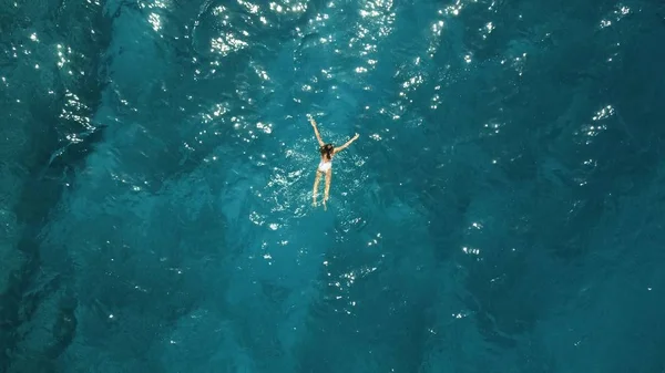 Vista aérea de cima para baixo de uma menina em um maiô branco nadando no mar azul — Fotografia de Stock