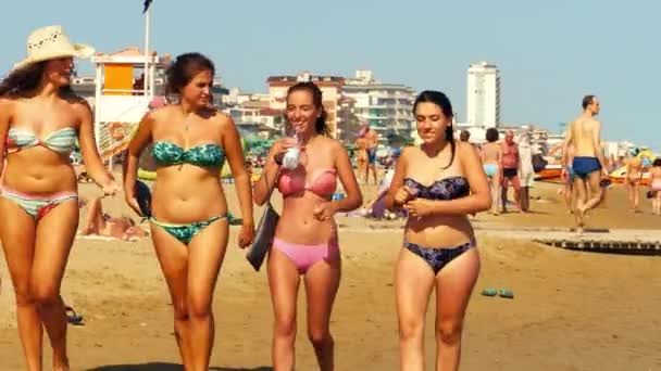 LIDO DI JESOLO, ITALIA - 8 de agosto de 2017. Mujeres jóvenes en bikini caminan por la abarrotada playa de arena — Vídeos de Stock
