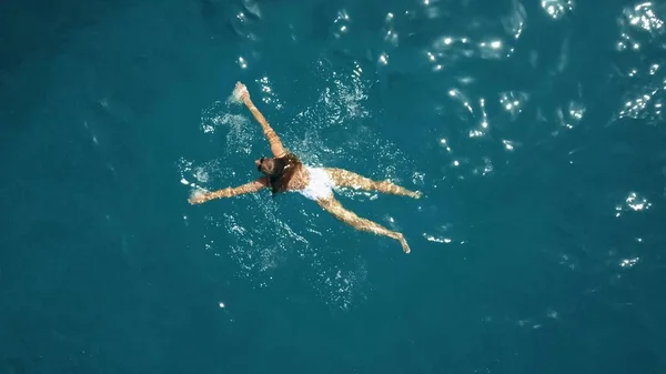 Antena z góry na dół widok młodej kobiety w biały strój kąpielowy pływanie w morzu — Zdjęcie stockowe
