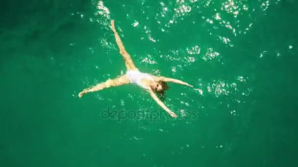 Vista aérea de cima para baixo de uma bela jovem mulher em um banho de maiô branco no mar — Vídeo de Stock