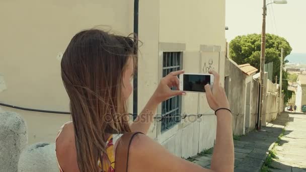 Young woman making photos of old Mediterranean town street with her smartphone — Stock Video