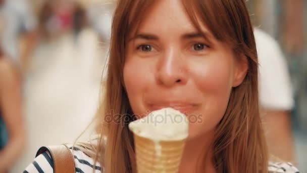 Glückliche junge Frau isst Eistüte und geht die Straße hinunter — Stockvideo