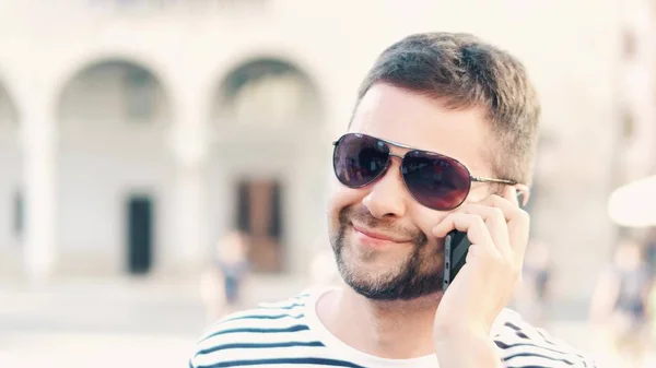 Junger schöner bärtiger Mann, der auf der Straße mit seinem Handy spricht — Stockfoto