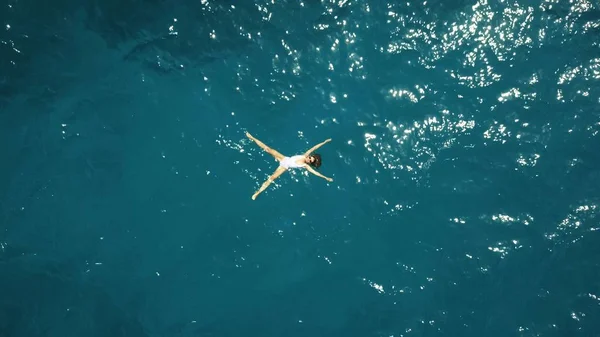 Aerial top down view of a beautiful young woman in a white swimsuit bathing in the blue sea — Stock Photo, Image