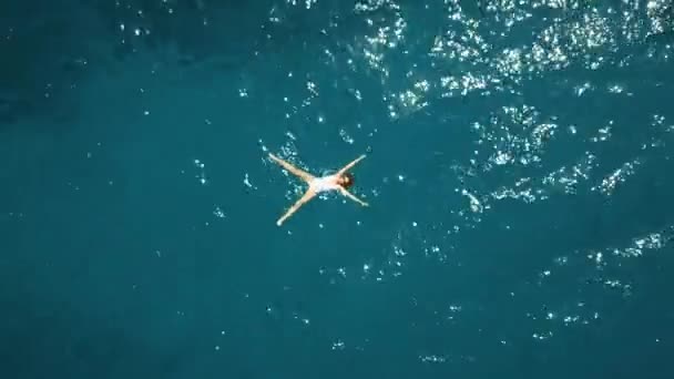 Vista aérea de cima para baixo de uma bela jovem mulher em um banho de maiô branco no mar azul — Vídeo de Stock