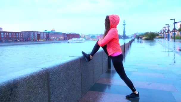 Молода змішана гонка атлетична бігунка зігрівається перед бігом вздовж набережної міського парку ввечері — стокове відео
