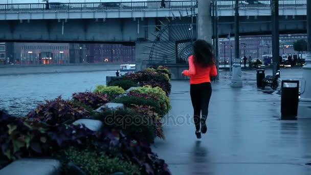 Joven corredora atlética de carrera mixta corriendo a lo largo del terraplén del parque de la ciudad por la noche, disparo en cámara lenta — Vídeo de stock