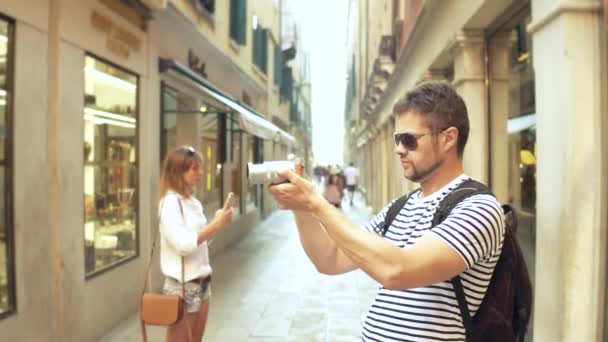 Jeune homme barbu beau faire des photos d'une rue étroite avec son appareil photo — Video