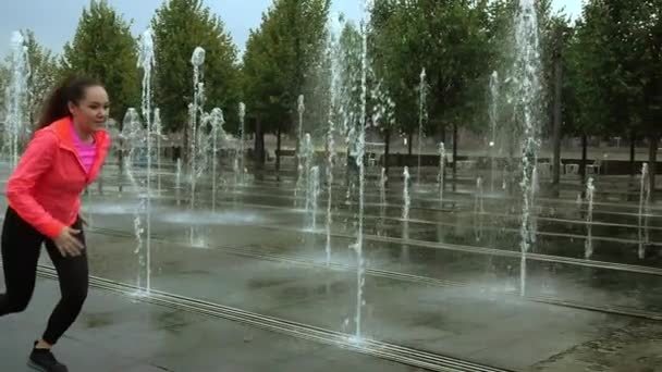 Jeune femme sportive mixte courir sous la pluie près des fontaines du parc de la ville, super ralenti vidéo — Video