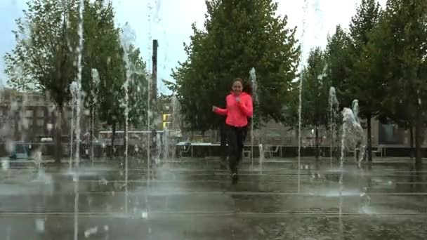 Jovem mista correndo na chuva perto de fontes do parque da cidade, tiro em câmera lenta — Vídeo de Stock