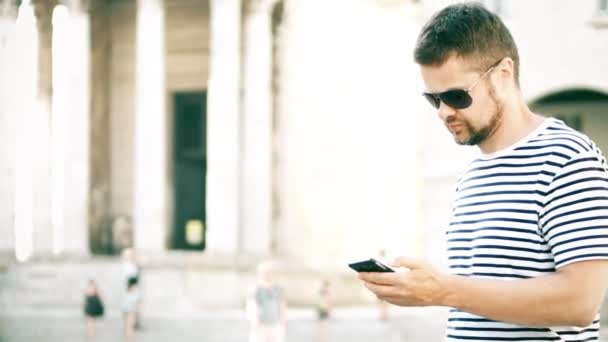 Молодой красивый мужчина пользуется своим смартфоном на улице — стоковое видео
