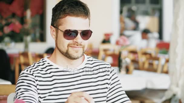 Young bearded man having coffee in a street cafe on his vacation — Stock Video