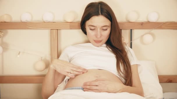 Krásná těhotná žena hladí její břicho v posteli — Stock video