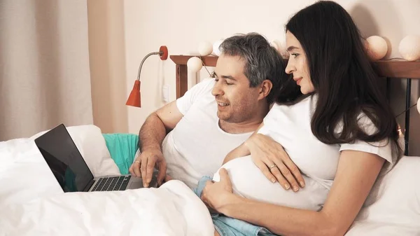 Marido e esposa grávida usando seu laptop na cama — Fotografia de Stock