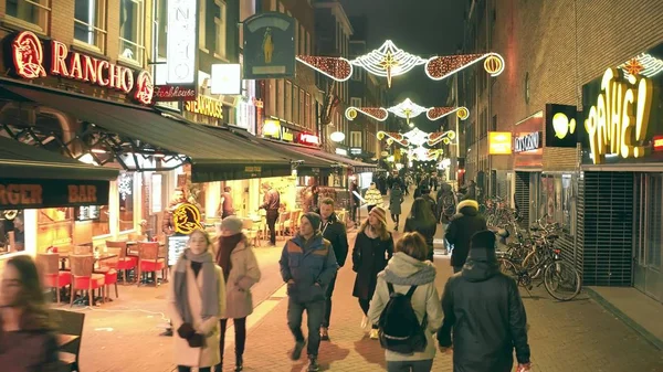 АМСТЕРДАМ, НИДЕРЛАНДЫ - 25 ДЕКАБРЯ 2017 года. Прогулка по переполненной туристической улице оформлены на Рождество и Новый год ночью — стоковое фото