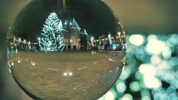 Неизвестные туристы ходят по площади украшенной на Рождество и Новый год вечером, просматривая стеклянный шар. Амстердам, Нидерланды — стоковое фото