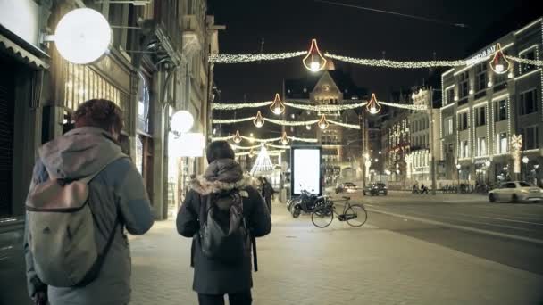 Amsterdam, Nizozemsko - 25 prosince 2017. Turisté s batohy procházkou po hlavní ulici, zdobené na Vánoce a nový rok — Stock video