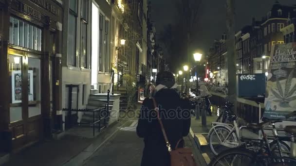 Amsterdam, Nizozemsko - 26 prosince 2017. Lidé chodí po nábřeží kanálu poblíž Muzeum marihuany večer — Stock video