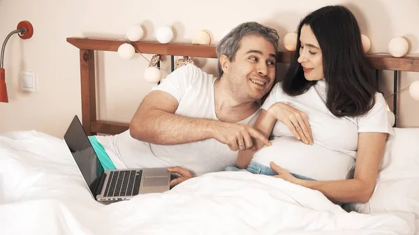 Man en zwangere vrouw online winkelen in het bed — Stockfoto