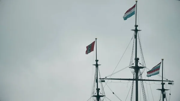 Acenando bandeiras dos Países Baixos e Amsterdã nos mastros de um antigo memorial de navios — Fotografia de Stock