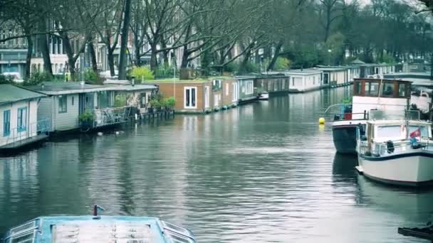AMSTERDAM, NETHERLANDS - DECEMBER 26, 2017. River tour boat and houseboats along city canal — Stock Video